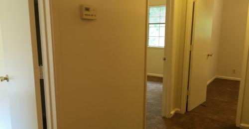 Hallway shows open doors, dark brown carpet.